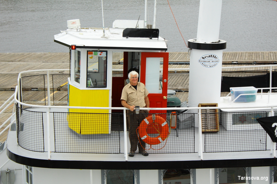 Капитан с кружкой кофе стоит на палубе, ожидая туристов